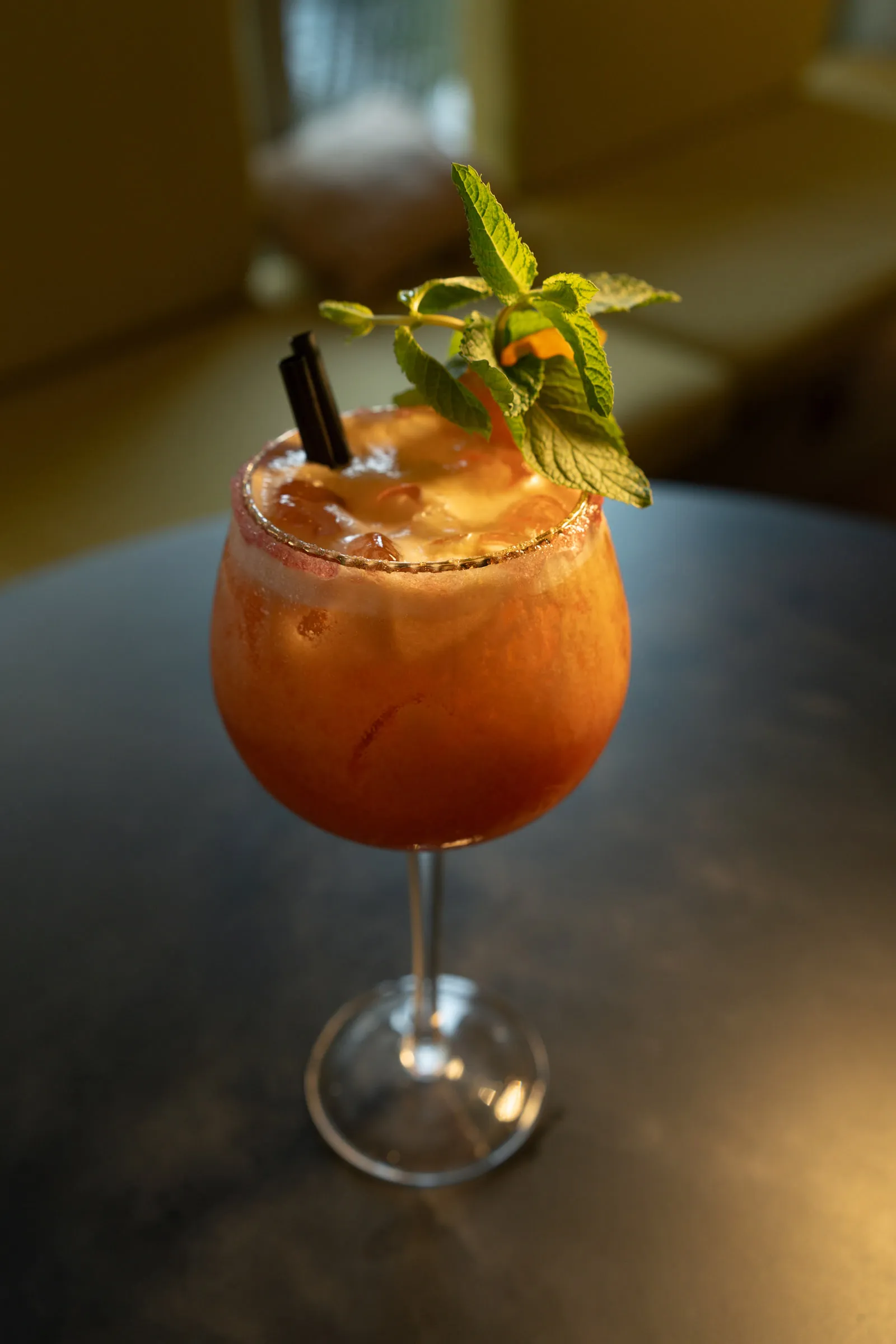 Orange mocktail in a stemmed glass with fresh mint and a black straw, on a dark table