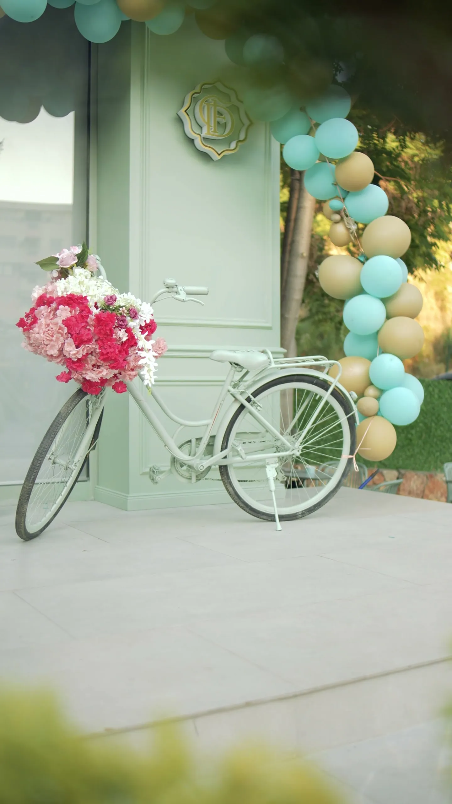 A white bicycle with a basket of pink and red flowers beside the sage door and the emblem