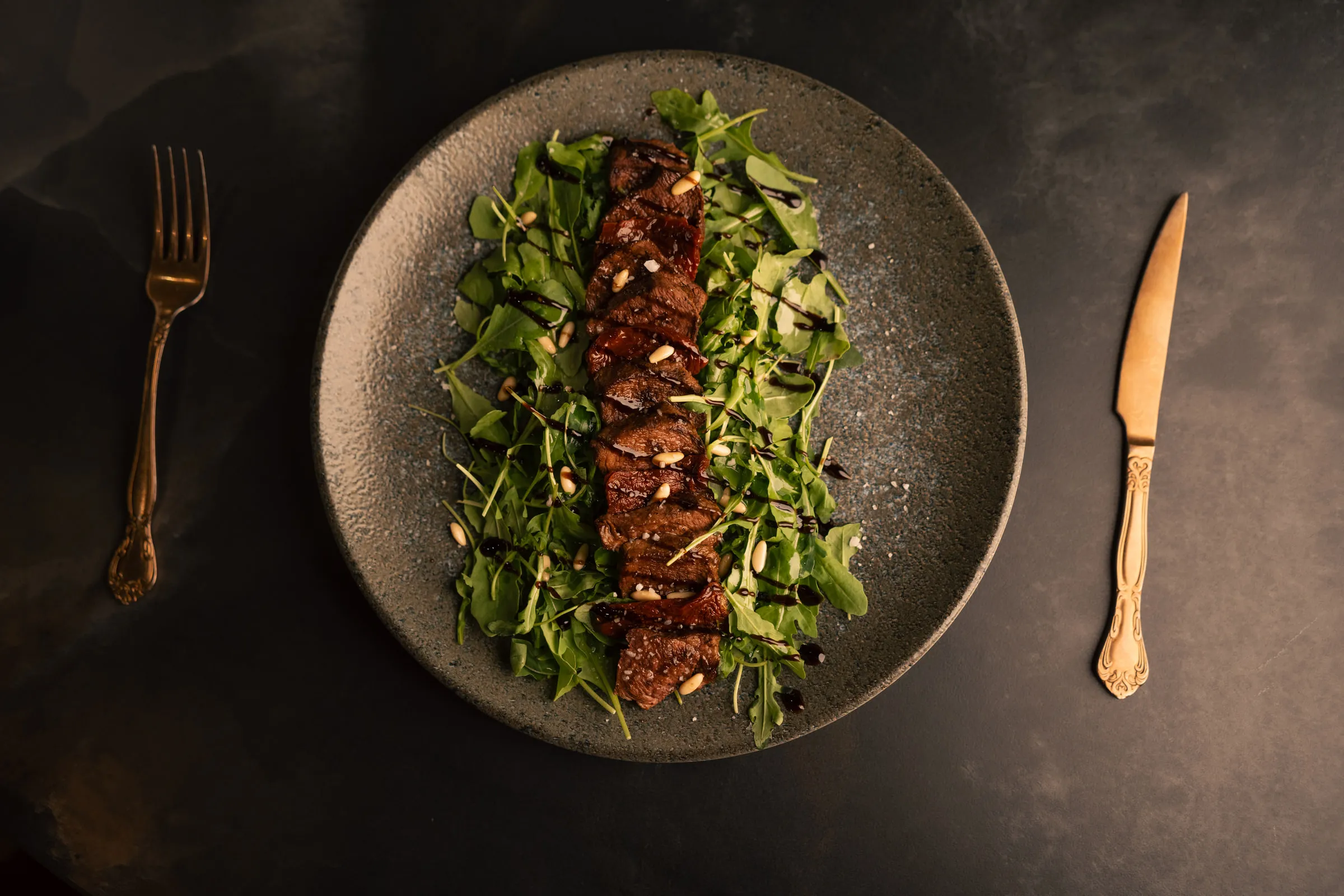 Beef tagliata on rocket with pine nuts and balsamic, seen from above with gold cutlery