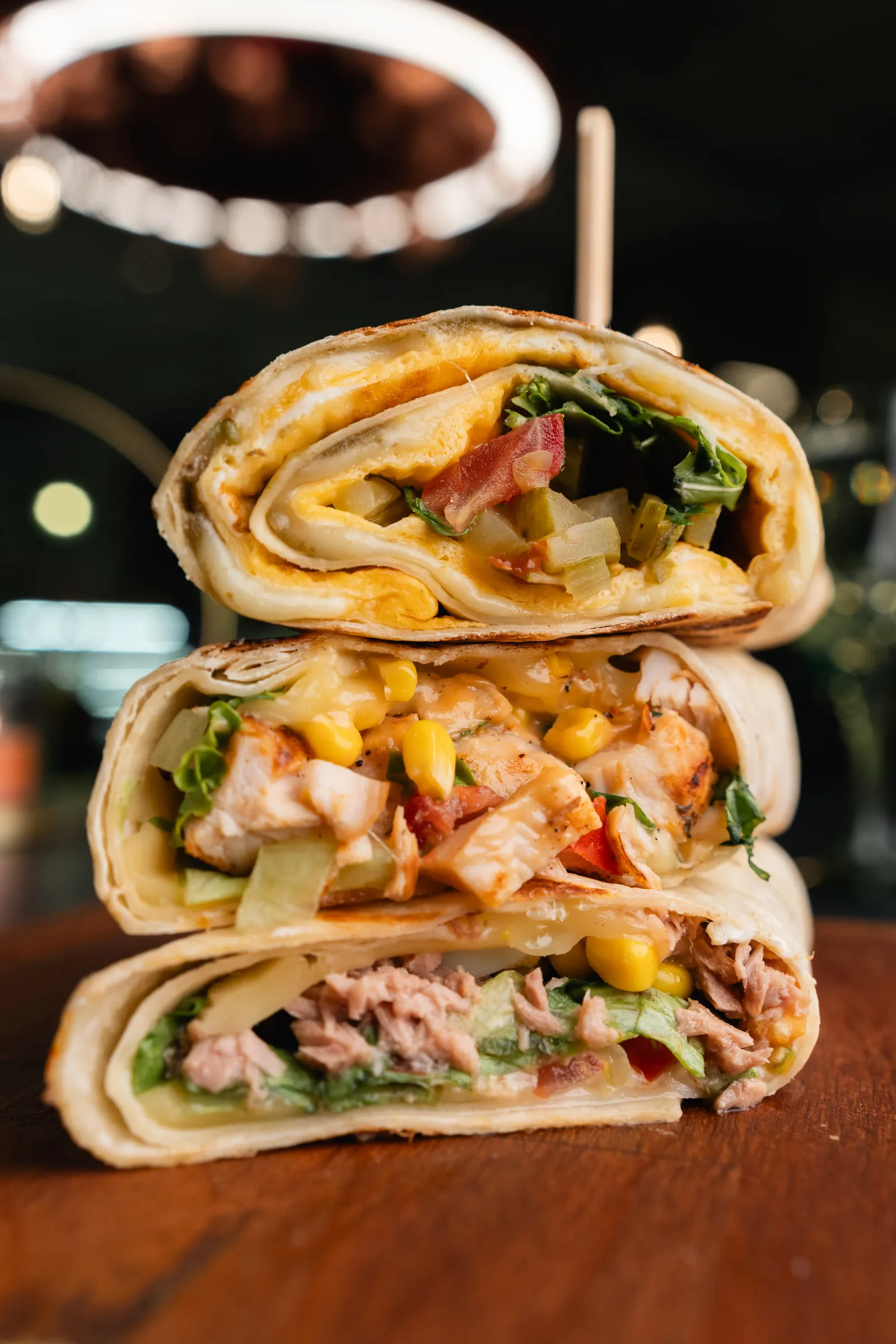 Three halves of breakfast burritos stacked to show the fillings, the flower chandelier glowing behind
